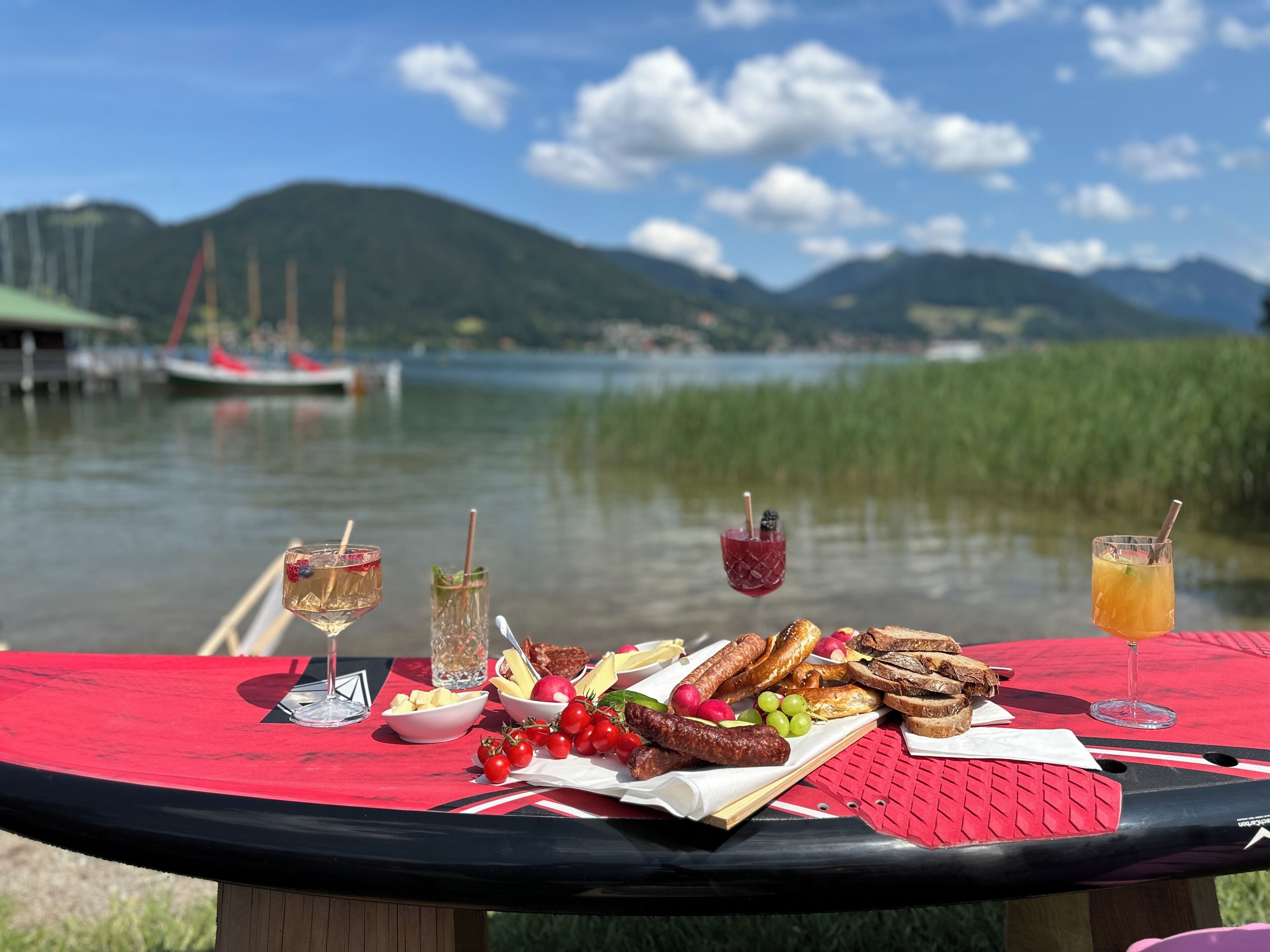 Une table de pique-nique avec de la nourriture et des boissons, près d’un lac où l’on aperçoit des bateaux au loin.