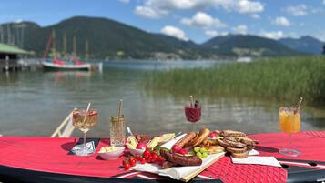 Une table de pique-nique avec de la nourriture et des boissons, près d’un lac où l’on aperçoit des bateaux au loin.