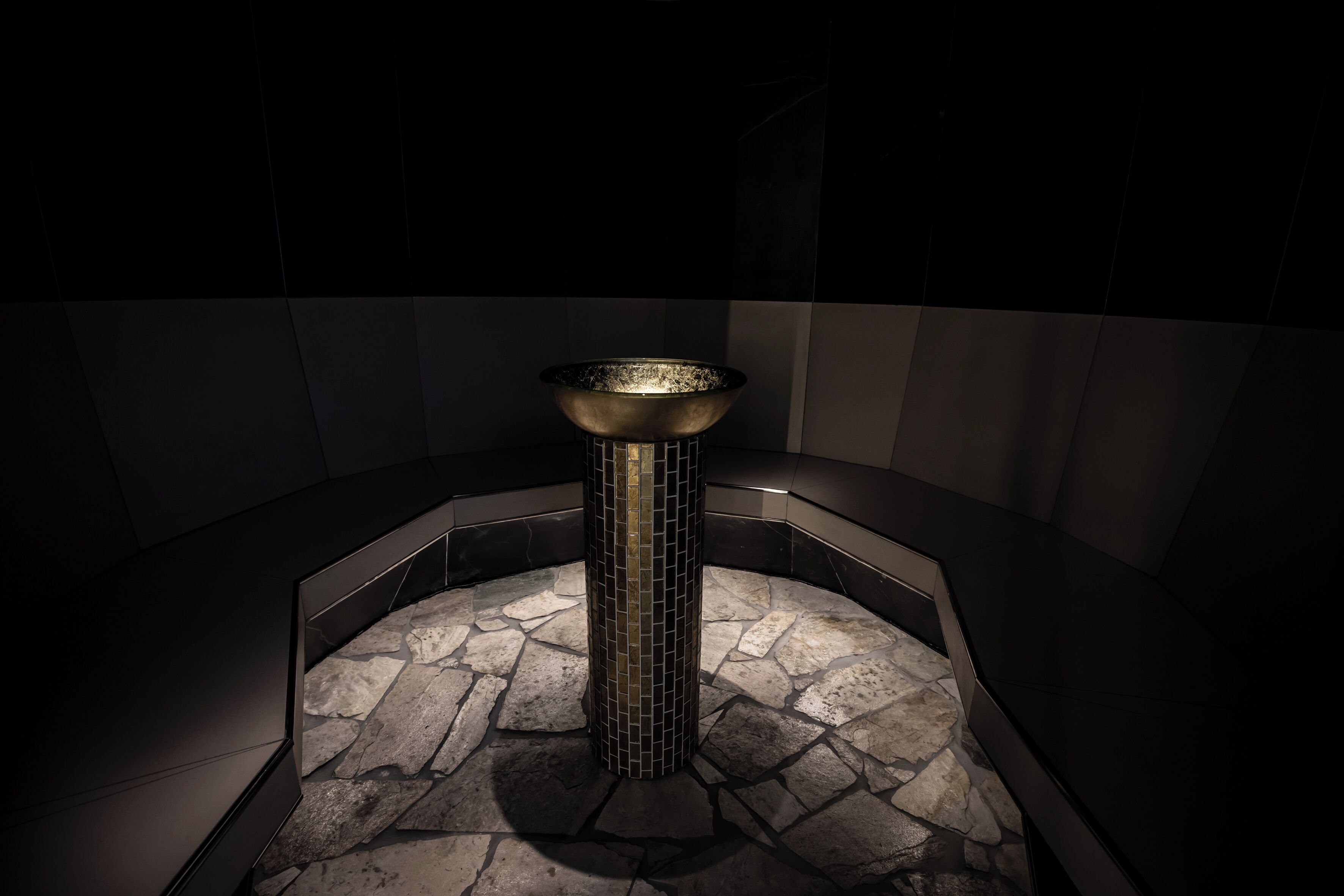 A modern bathroom with a central column, stone flooring, and dark walls.
