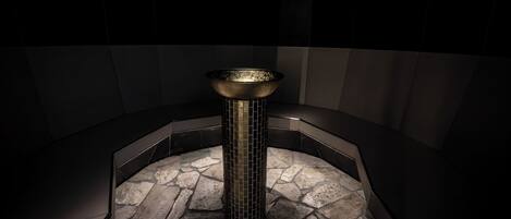 A modern bathroom with a central column, stone flooring, and dark walls.