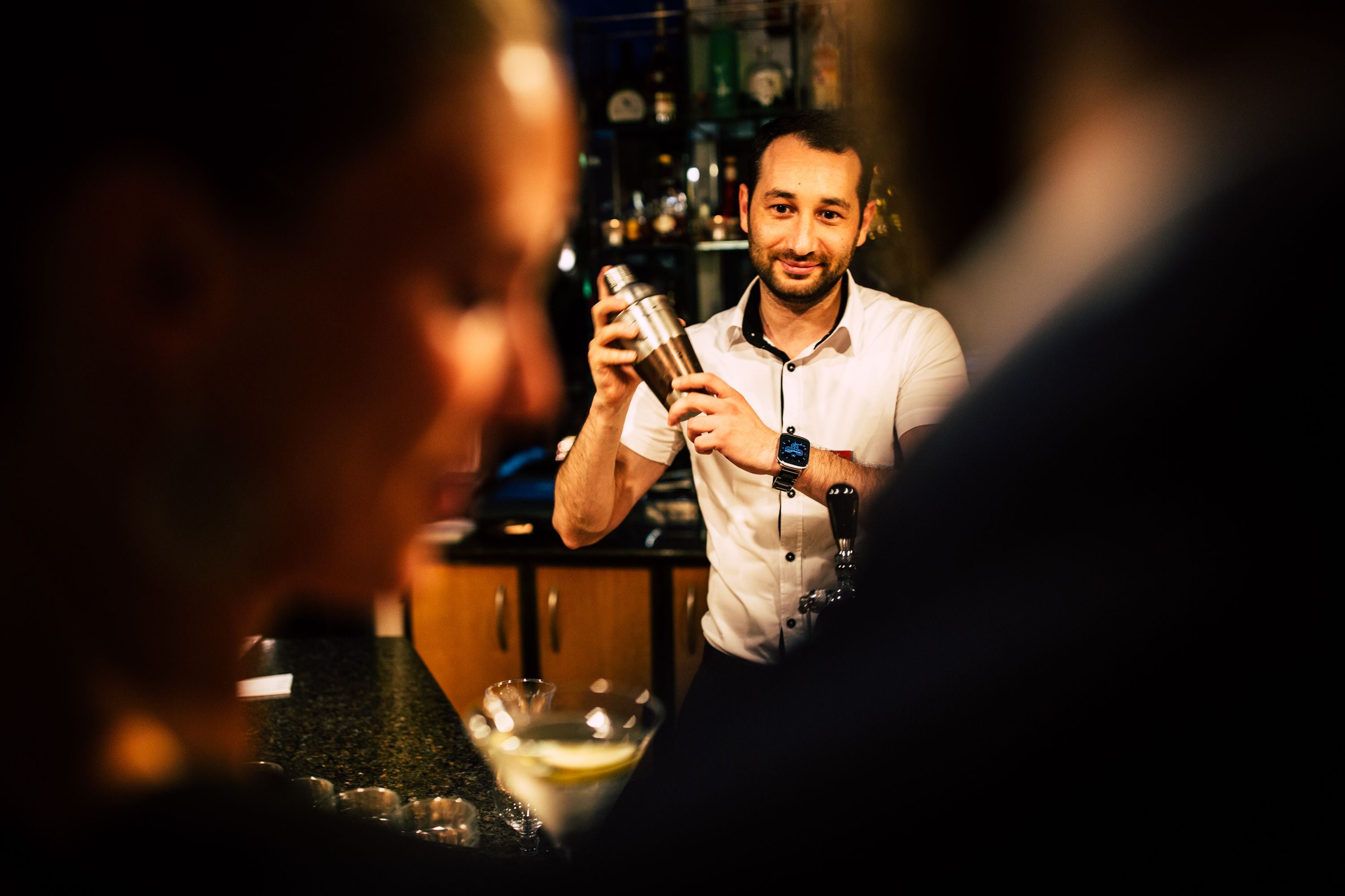 Un bartender preparando una bebida detrás de la barra, con varias botellas y vasos.