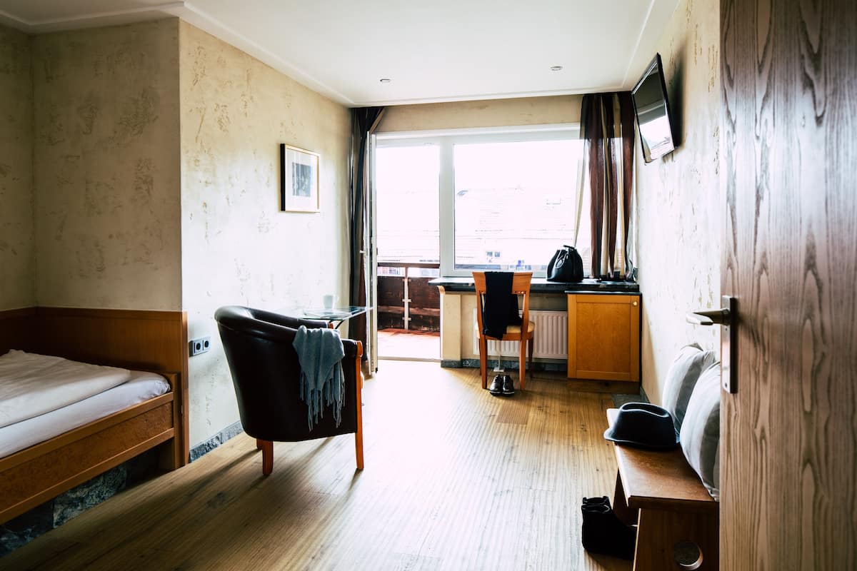 A hotel room with a bed, a chair, a small table, a television, and a view of the outside.