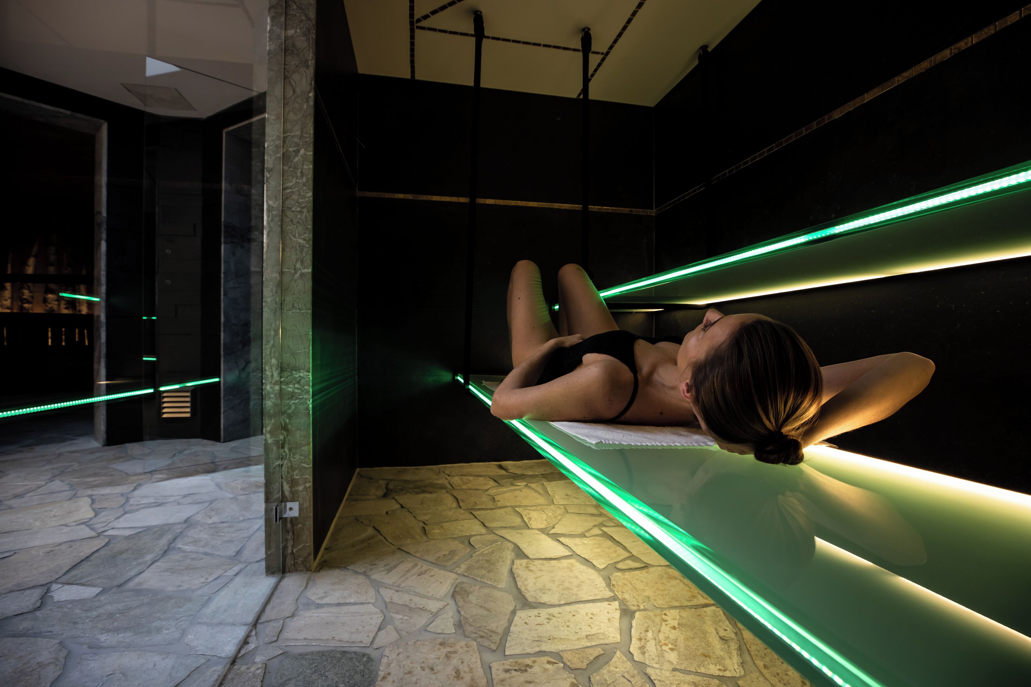 A room with a stone floor, a bed with green underlighting, and a dark wall.