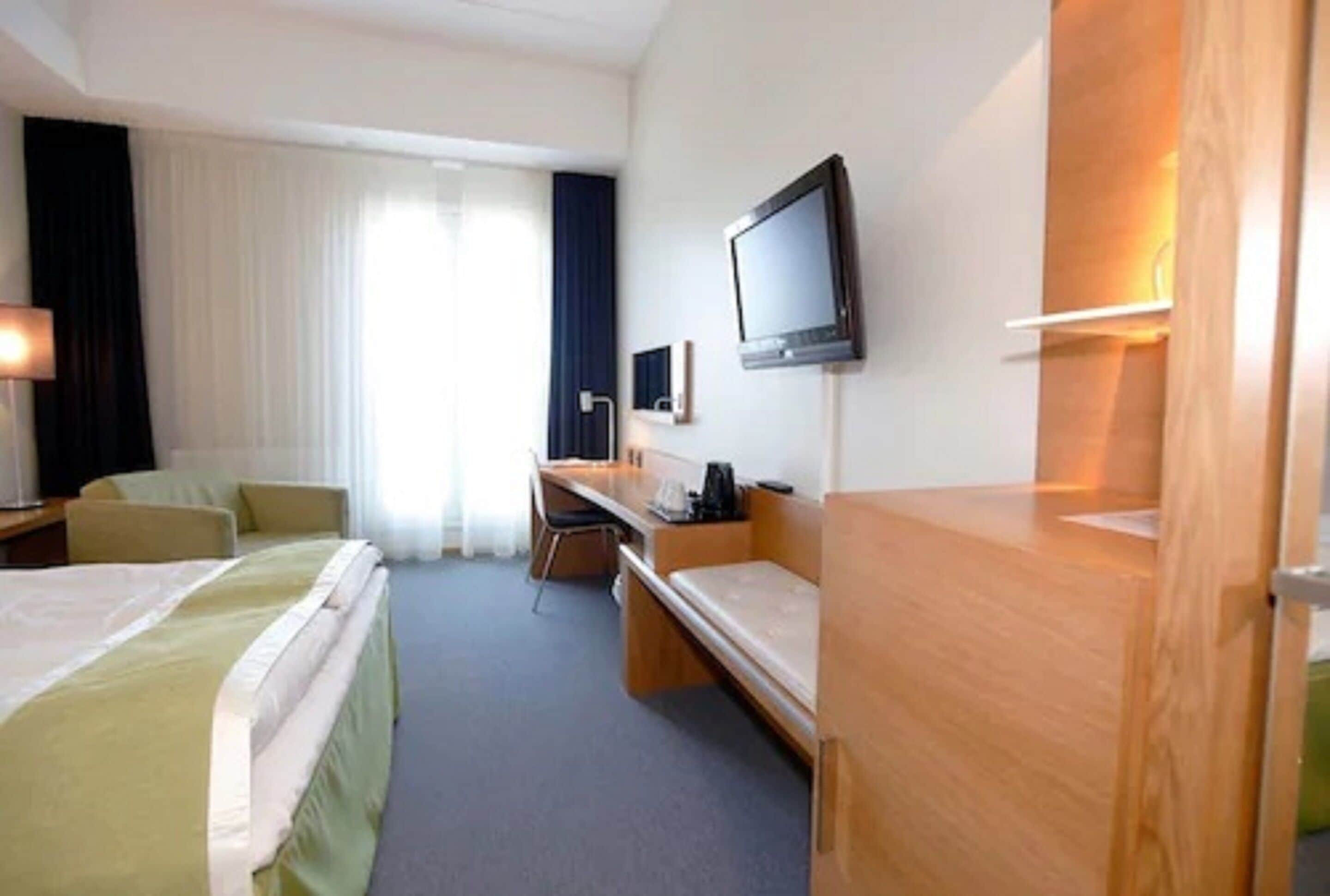 A hotel room with two beds, a desk, a chair, a television, and a window with curtains.