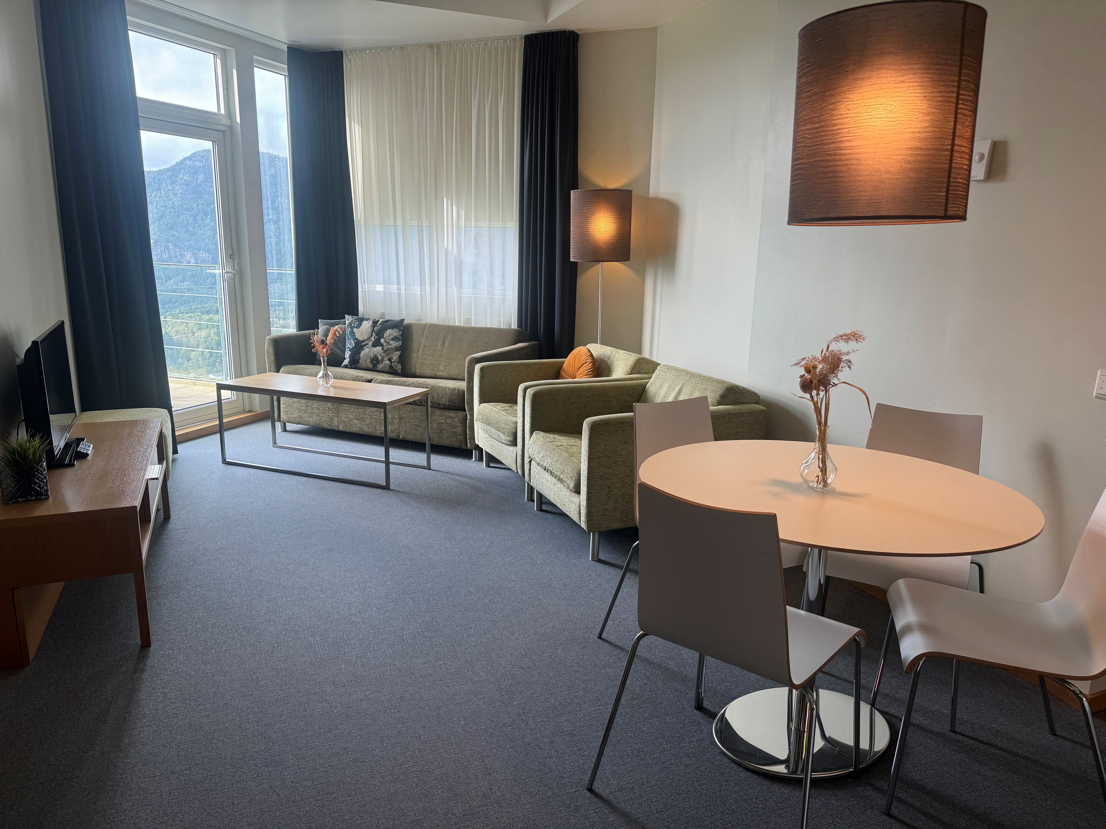Quarto de hotel moderno com sofá, mesa de jantar e luminária.