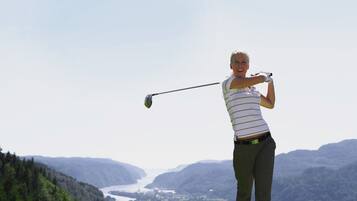 Una persona jugando golf en un campo verde con una vista panorámica de montañas y un río al fondo.
