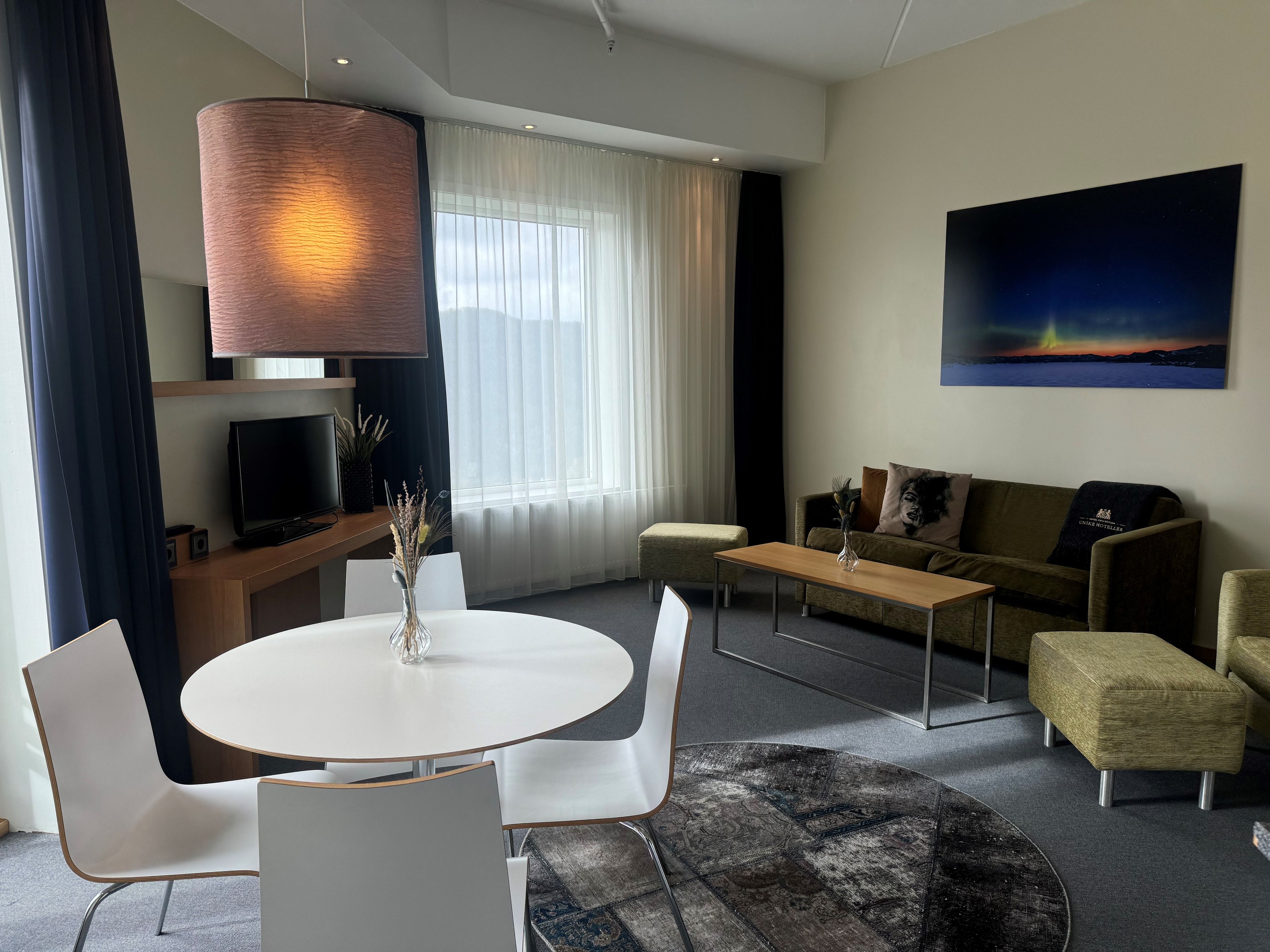 A modern living room with a round dining table, white chairs, a sofa, and a television.