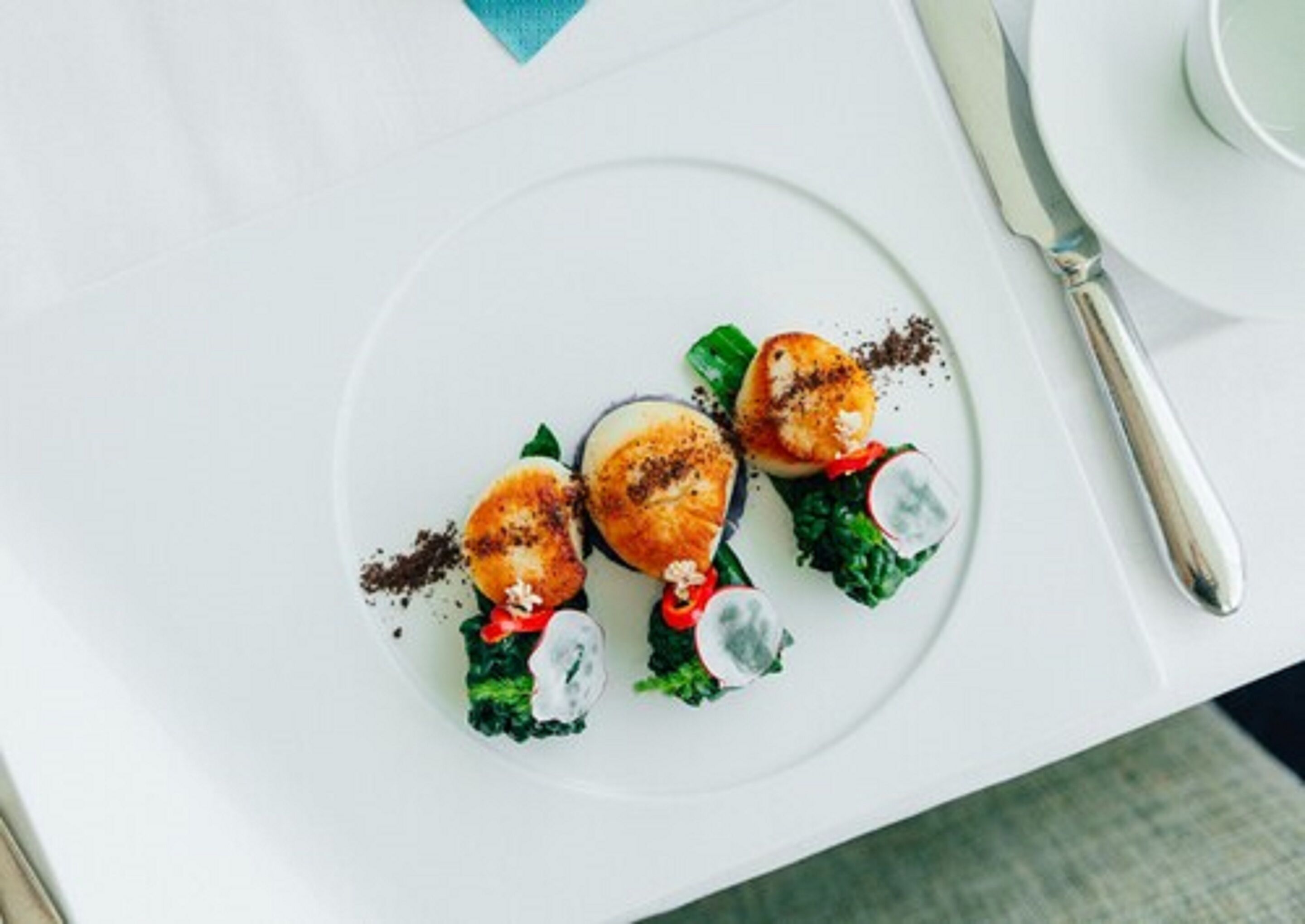 A white plate with three scallops, some greens, and a small red flower.