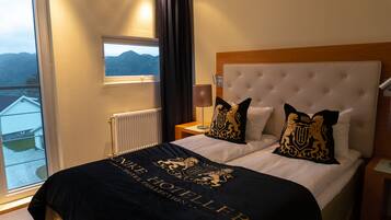 A hotel room with a large window, a bed with a black and gold throw, and a view of the mountains.