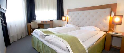 A hotel room with a large bed, a desk, two bedside lamps, and a window with curtains.