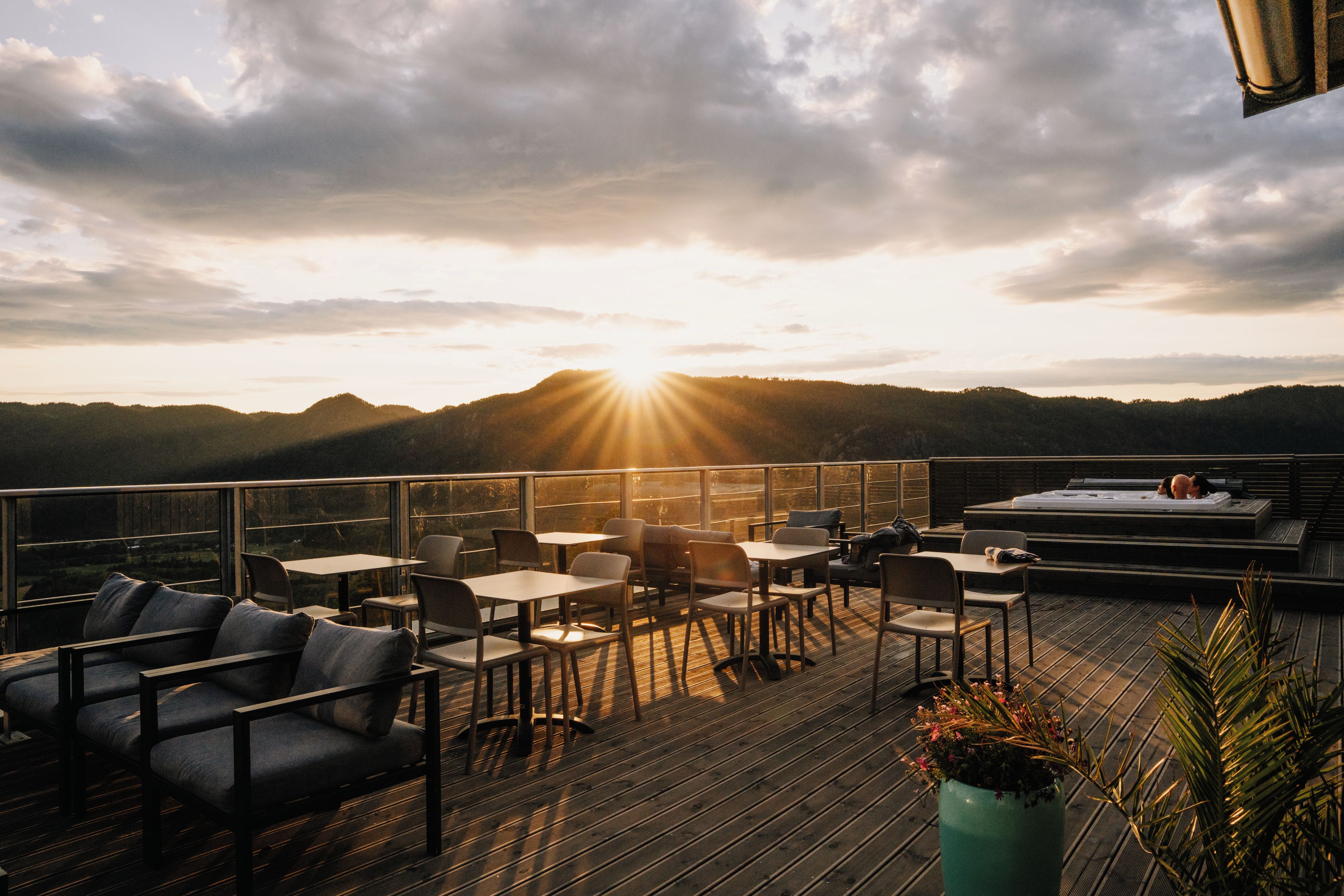 A terrace with tables and chairs, a hot tub, and a view of the mountains.