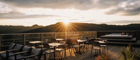 A terrace with tables and chairs, a hot tub, and a view of the mountains.