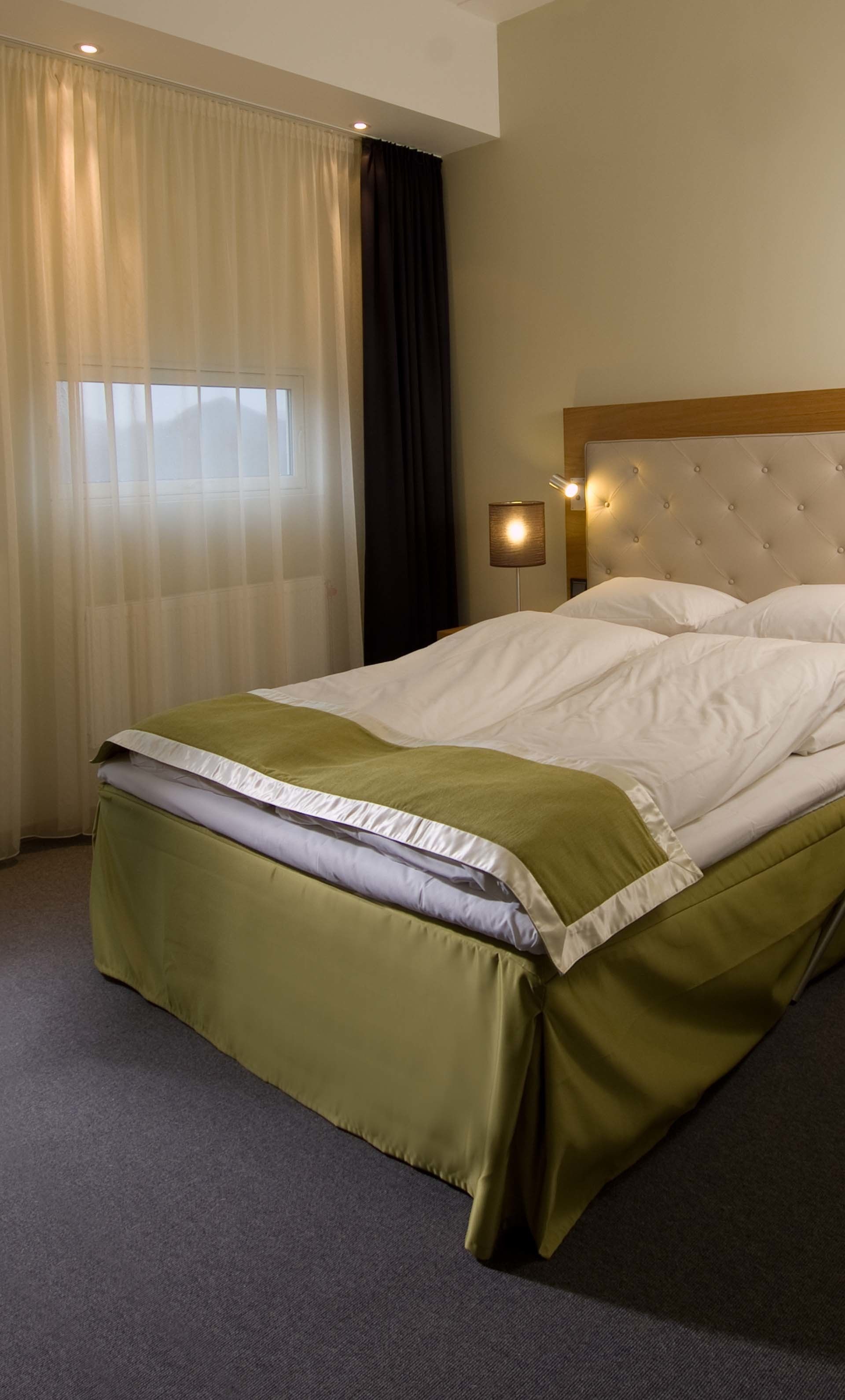 A hotel room with a bed, curtains, a nightstand, and a lamp.
