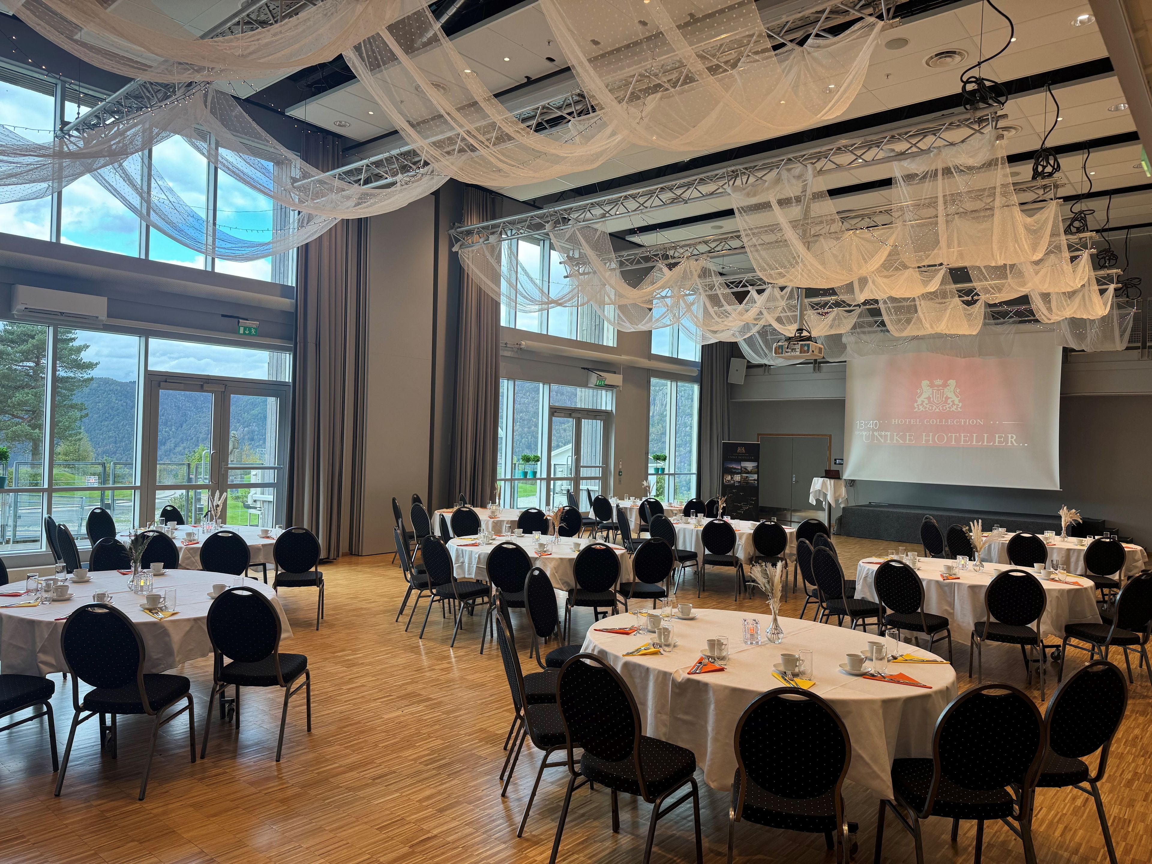 Une salle de conférence équipée de tables rondes, de chaises et d’un écran de projection.