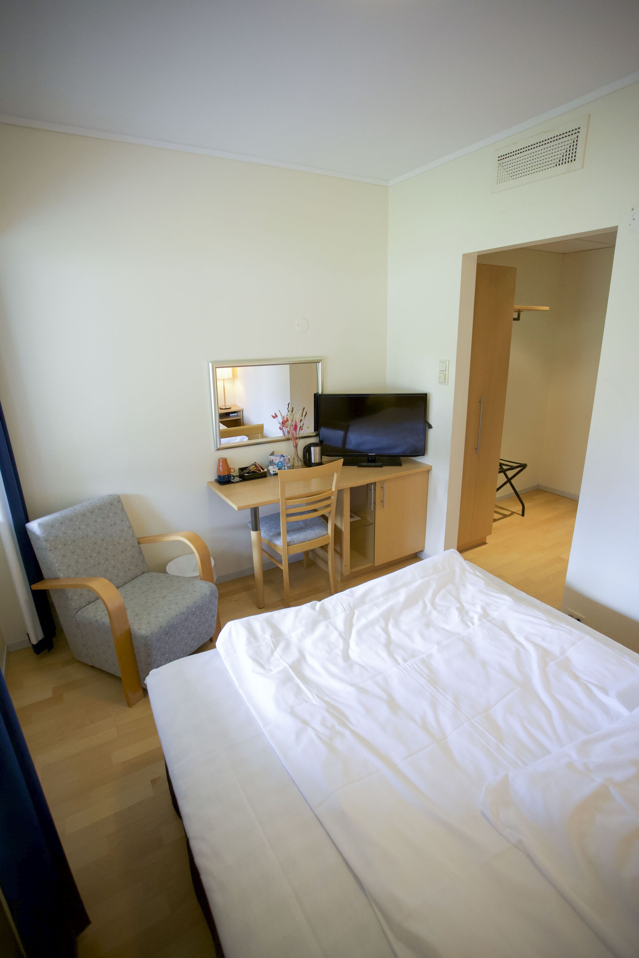A hotel room with a bed, a desk with a chair, a television, and a mirror.