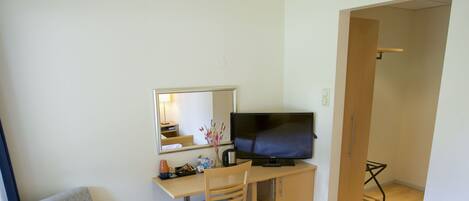 A hotel room with a bed, a desk with a chair, a television, and a mirror.