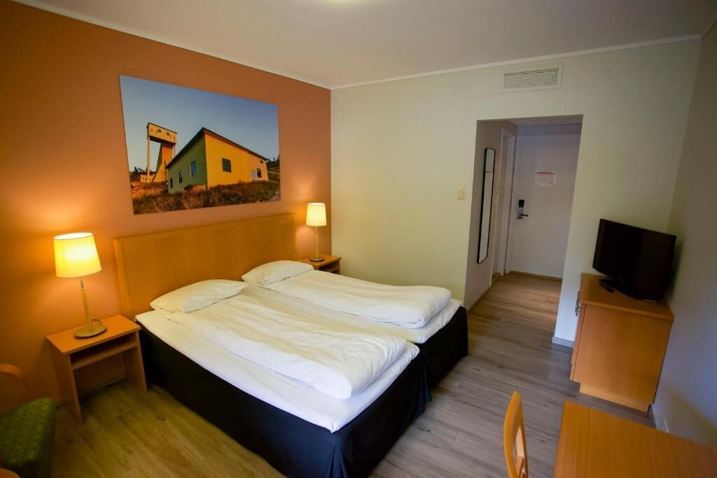 Una habitación de hotel con una cama, dos lámparas de noche, un televisor y un cuadro en la pared.
