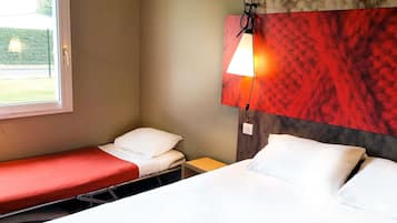 A hotel room with a single bed, a small bedside table, a window, and a wall-mounted lamp.