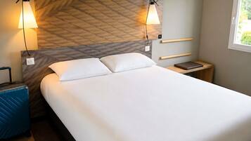 A hotel room with a bed, bedside tables, a suitcase, and a window.
