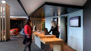 A modern reception desk with a computer, a seating area with red cushions, and a wall-mounted information board.