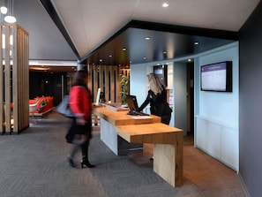 A modern reception desk with a computer, a seating area with red cushions, and a wall-mounted information board.