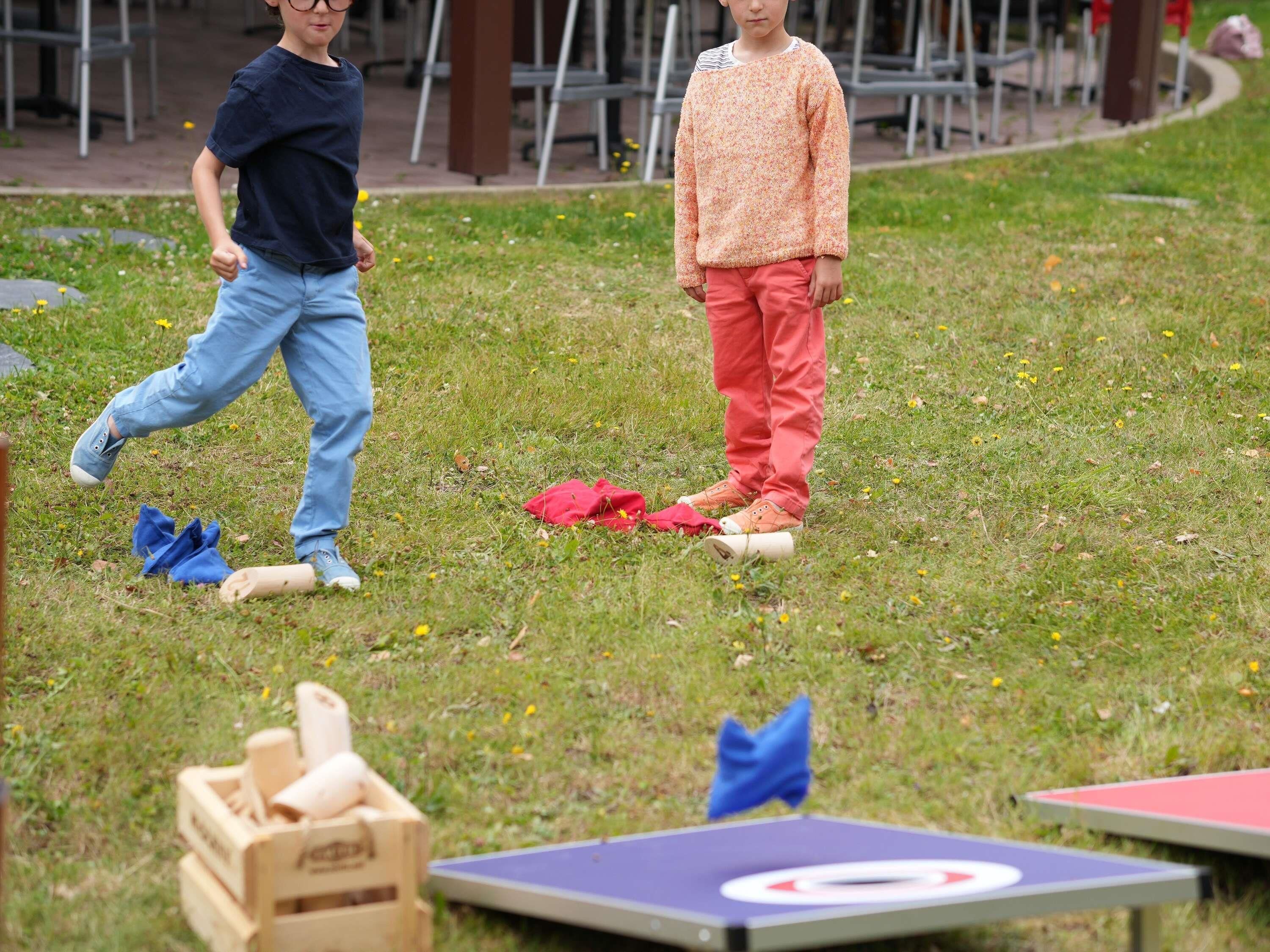 Dos personas de pie sobre césped, con una mesa de ping pong y objetos dispersos al frente.
