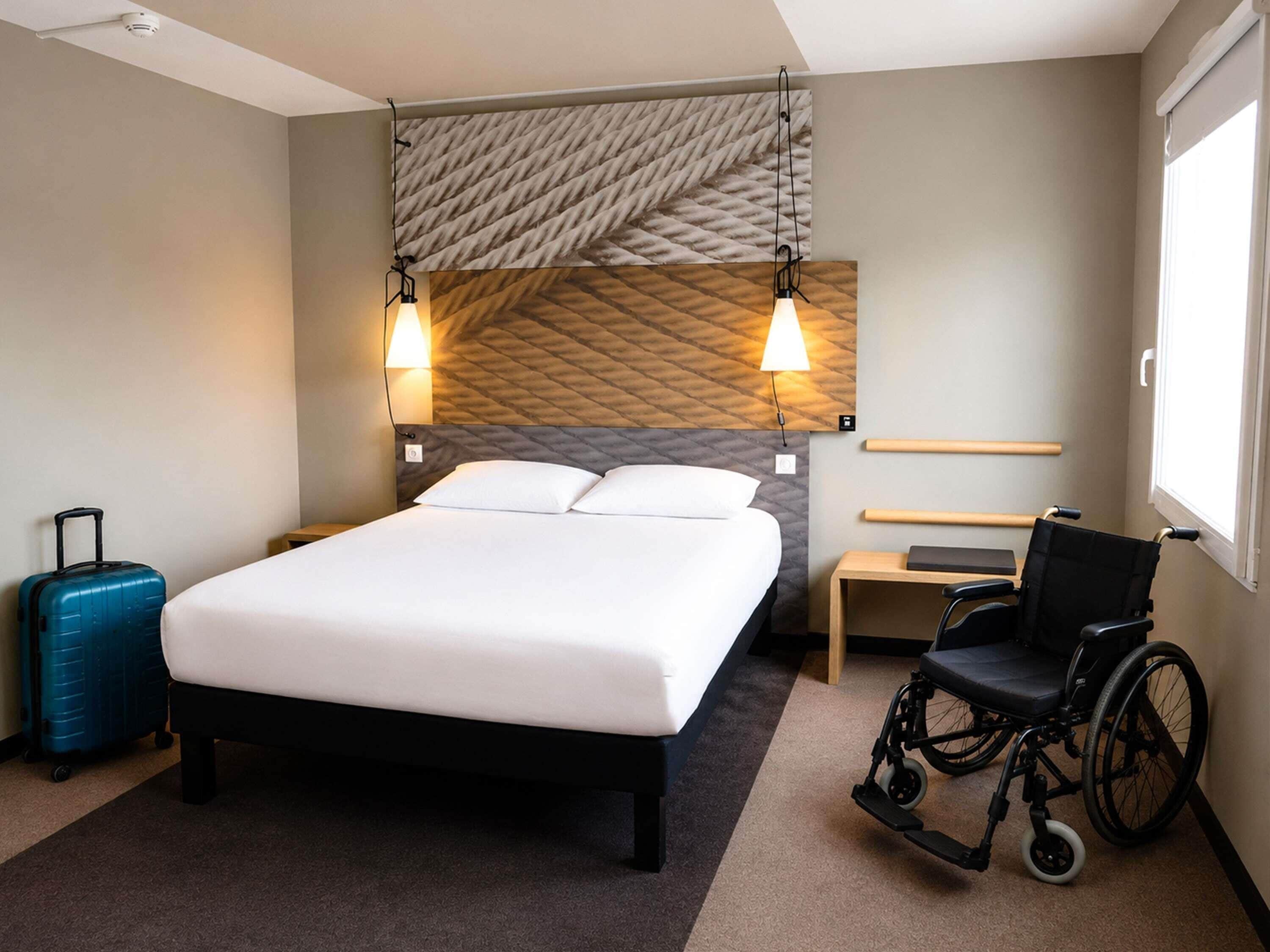 Una camera d'albergo con un letto, una sedia a rotelle, una valigia e una finestra.