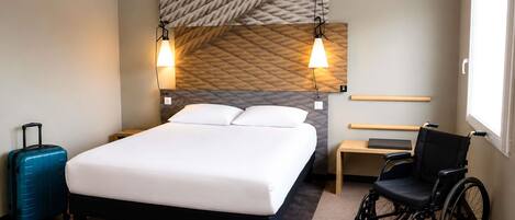 Habitación de hotel con cama, silla de ruedas, maleta y ventana.