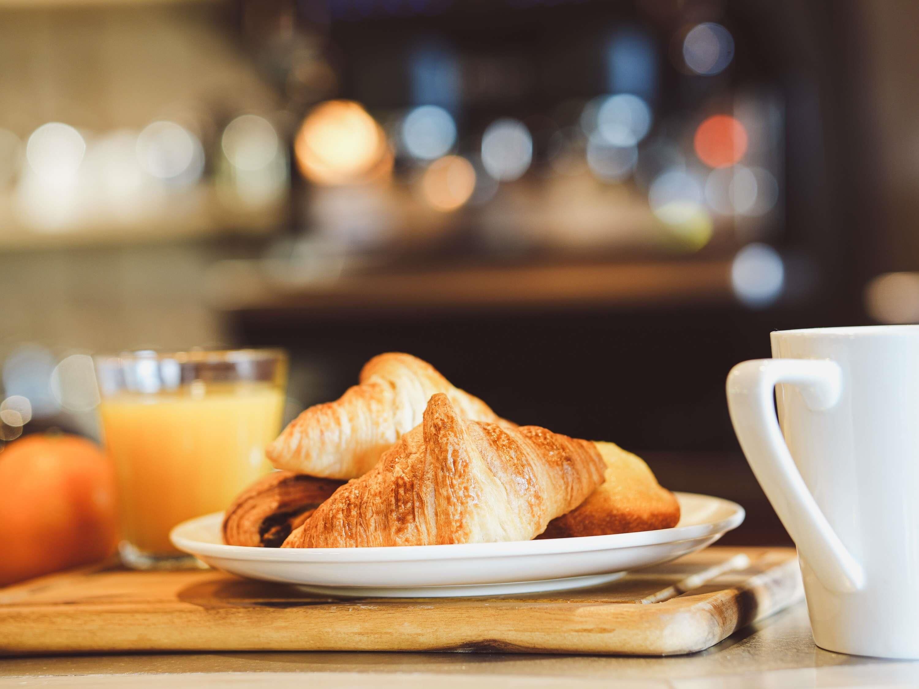 Un plato con croissants y un vaso de zumo de naranja sobre una superficie de madera.