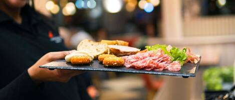 Una persona sosteniendo una bandeja con diferentes alimentos, entre ellos pan, croquetas y embutidos.