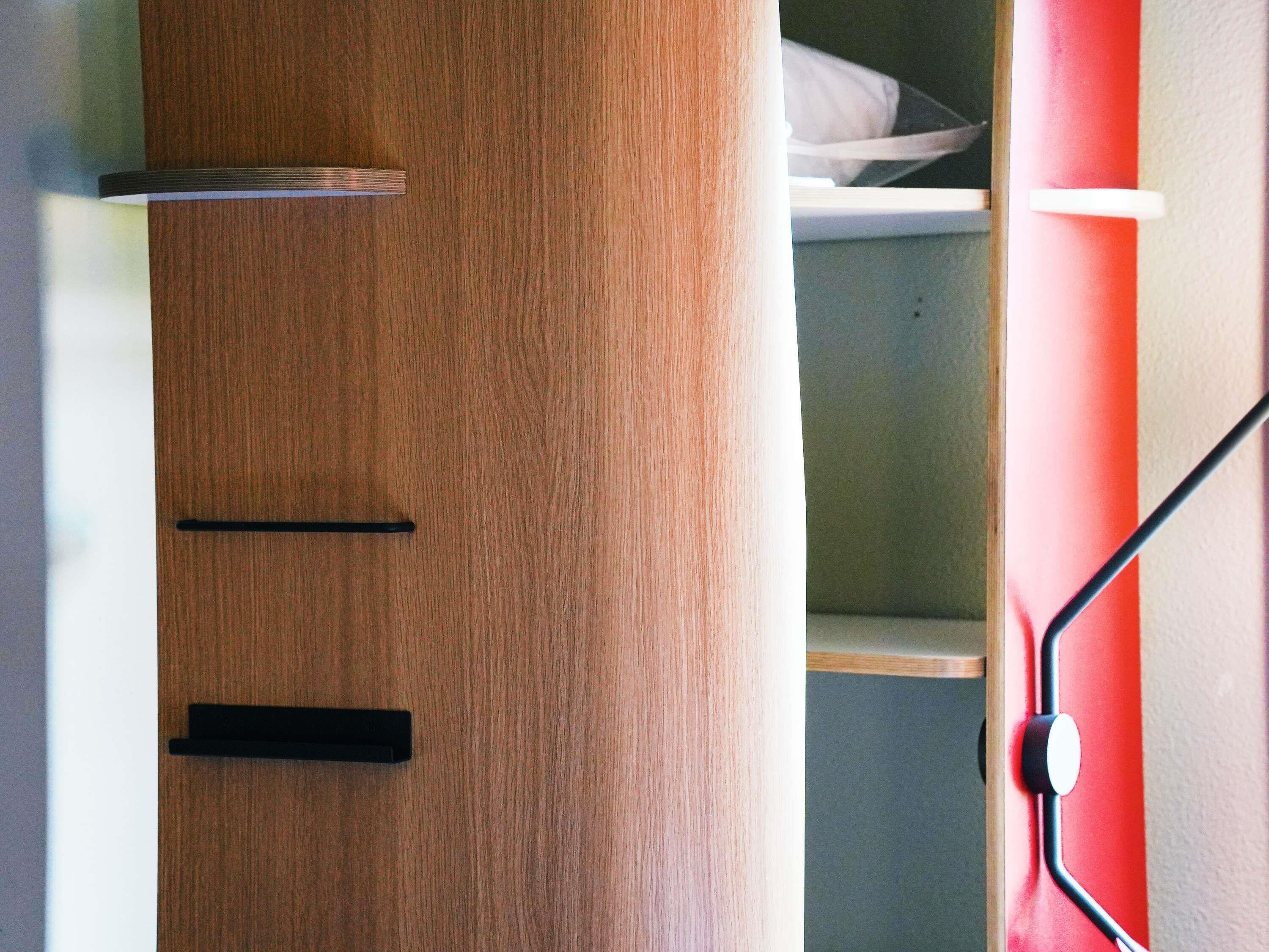 A wooden wardrobe with two drawers and a shelf, a red wall, and a black door handle.