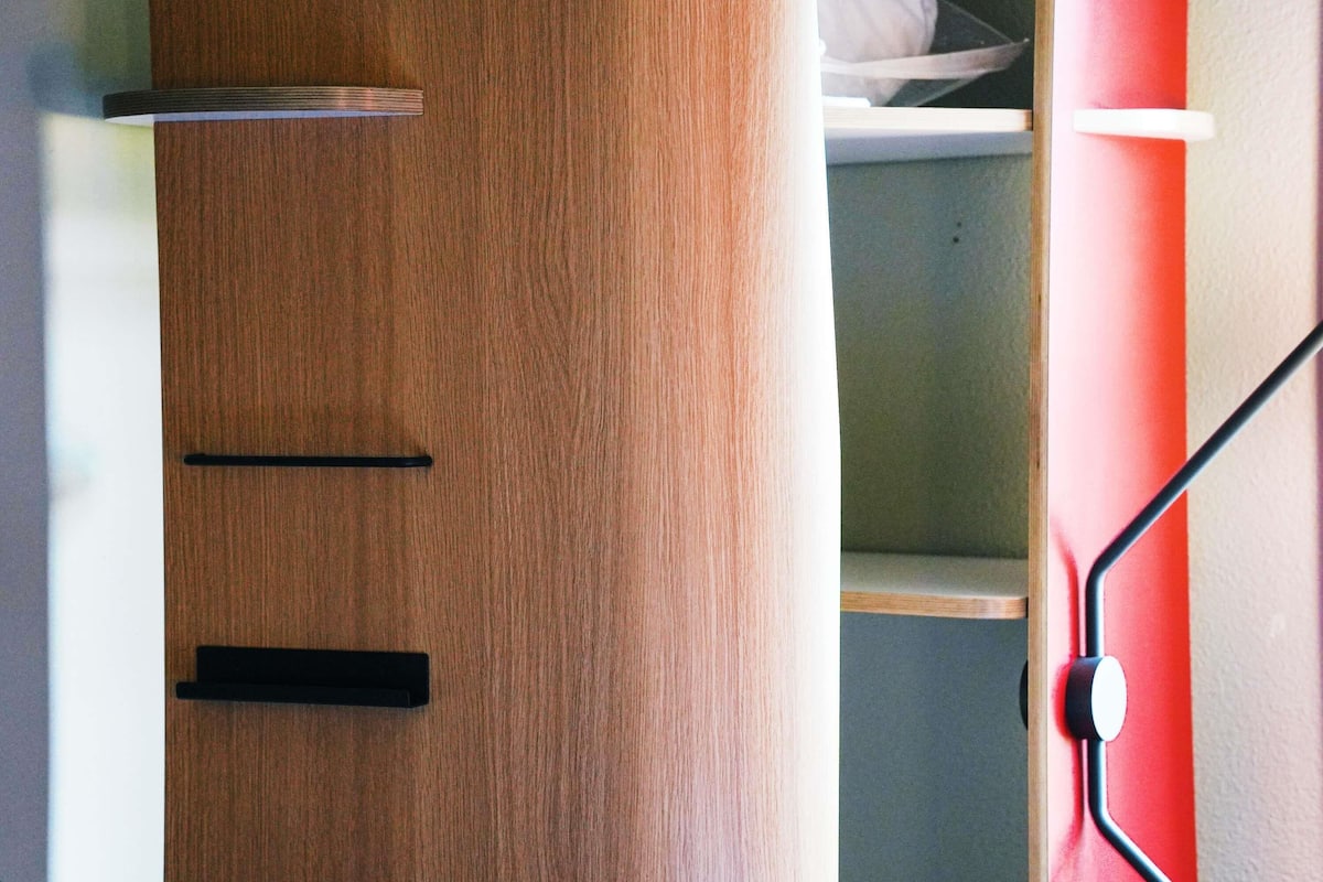 A wooden wardrobe with two drawers and a shelf, a red wall, and a black door handle.