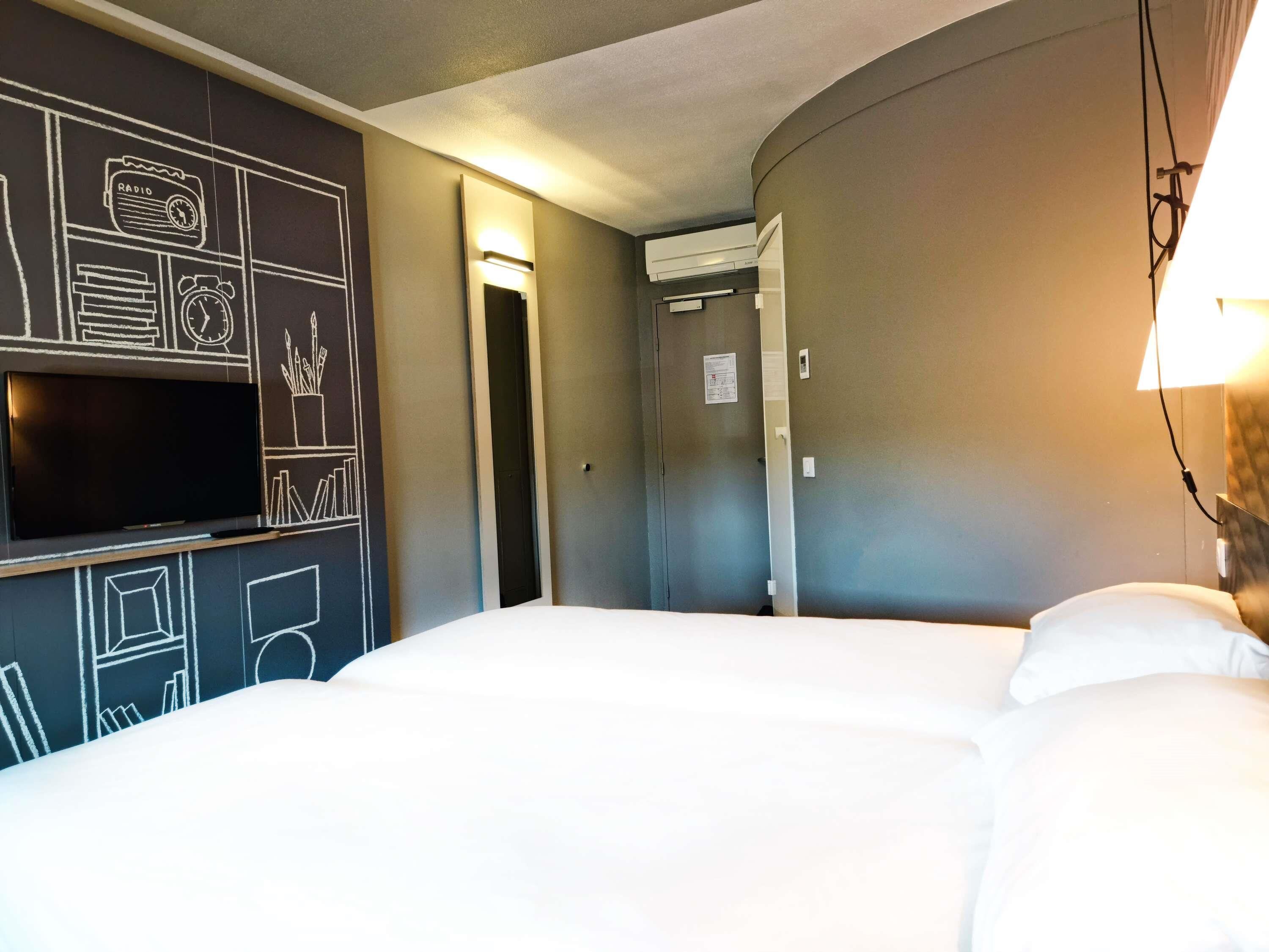 A hotel room with a bed, a TV mounted on the wall, and a door leading to another room.