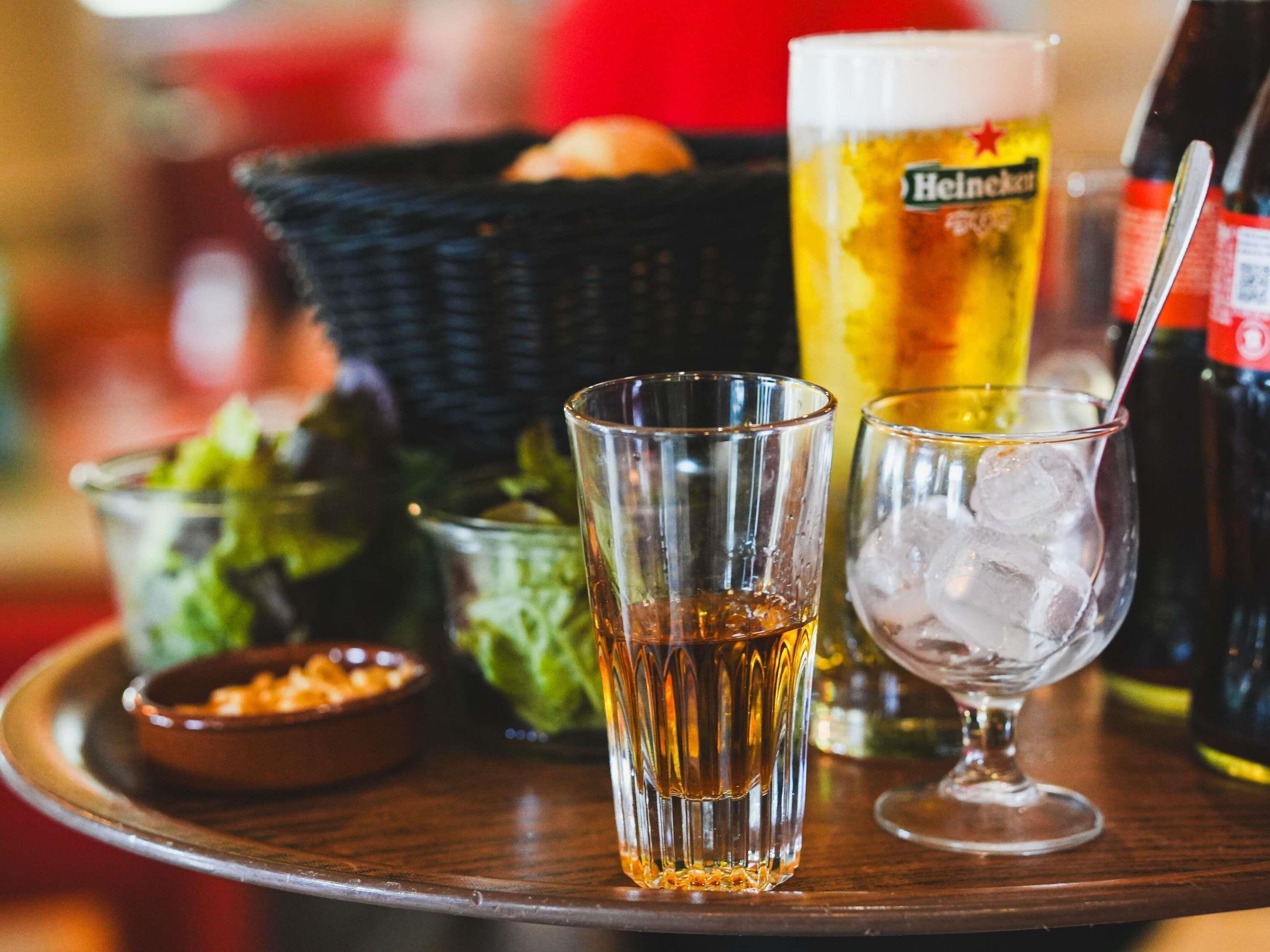 A tray with a glass of beer, a glass with ice, a bowl of salad, and a bottle of Heineken beer.