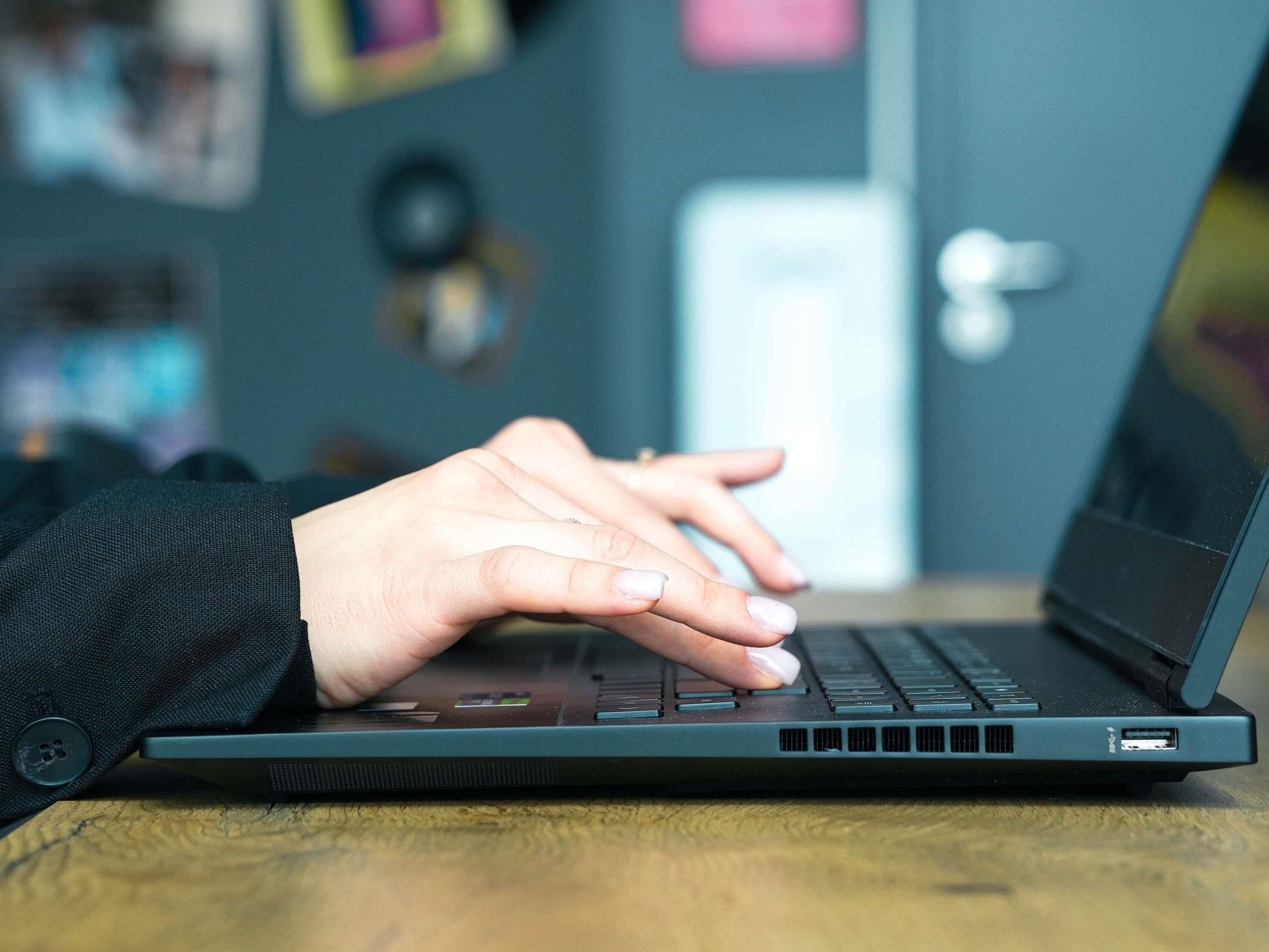 A laptop on a wooden surface with a person's hands typing on the keyboard.