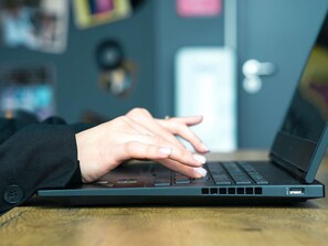 Un ordinateur portable posé sur une surface en bois, avec les mains d’une personne tapant sur le clavier.