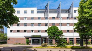 A B&B hotel with a modern design, featuring a brick facade and multiple flags. - B&B HOTEL Hamburg-Airport (Hamburg)
