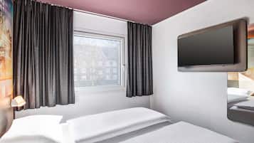 Une chambre d’hôtel avec deux lits, une fenêtre avec des rideaux, un téléviseur à écran plat fixé au mur et un tableau accroché au mur.