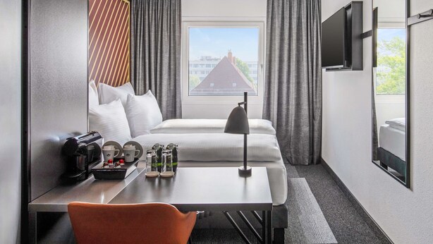 A hotel room with a bed, a desk with a chair, a coffee maker, and a TV mounted on the wall. - B&B HOTEL Hamburg-Airport (Hamburg)