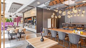 A modern restaurant with wooden tables and chairs, pendant lighting, and a bar area. - B&B HOTEL Hamburg-Airport (Hamburg)