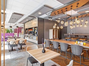 Un restaurante moderno con mesas y sillas de madera, iluminación colgante y una zona de bar.