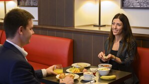 Een eethoek met een tafel gedekt voor twee personen, compleet met borden eten, een glas sinaasappelsap en een banaan.
