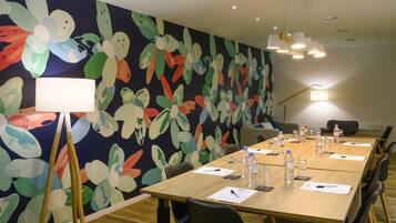 A conference room with a long table, chairs, a floral wall mural, and ceiling lights.