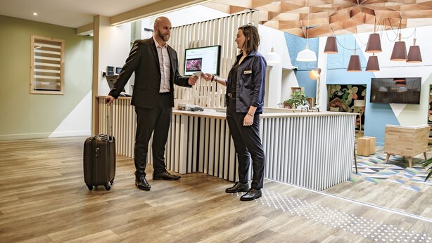 Een receptiezone met een houten vloer, een receptiebalie en een televisiescherm.