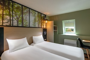 Habitación de hotel con una cama grande, un escritorio, una silla, una ventana y una obra de arte colgada en la pared.