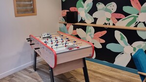 Una habitación con mesa de fútbol, estante en la pared y ventana con persianas.