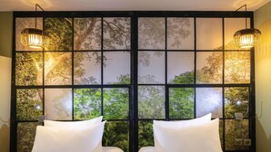 Een kamer met twee bedden, een groot raam met uitzicht op bomen, en twee wandlampen.