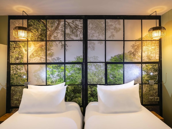 Une chambre avec deux lits, une grande fenêtre donnant sur la verdure et deux lampes fixées au mur.