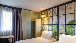 Hotelkamer met twee bedden, een bureau, een stoel en een groot raam met uitzicht op bomen.