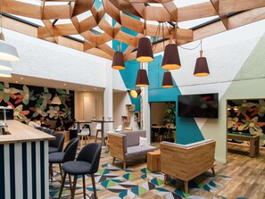 A modern lounge area with a bar, seating, and a large TV screen. - ibis Styles Parc des Expositions de Villepinte (Villepinte)